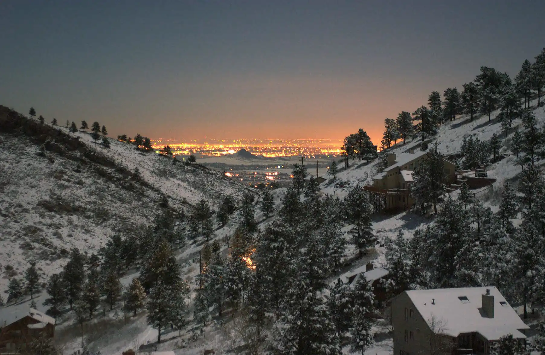 Boulder's city lights glowing below the snow-dusted foothills at dusk